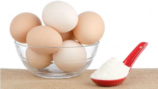 a bowl of whole boiled eggs next to a measuring spoon filled with egg protein powder